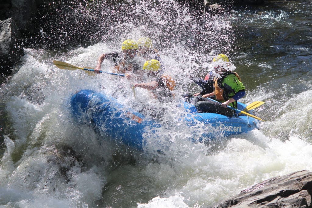 Blue raft hitting wave on Clear Creek and splashing four people wearing helmets and holding paddles