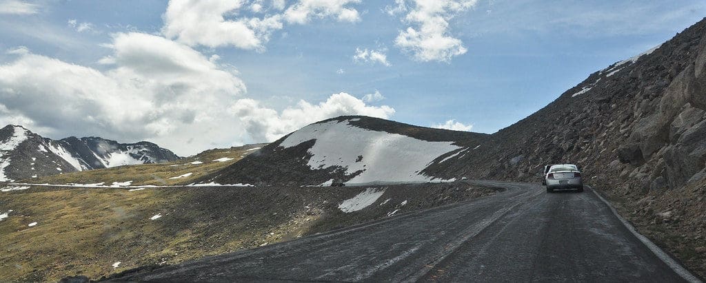 Paved road with two cars on high alpine pass with some snow