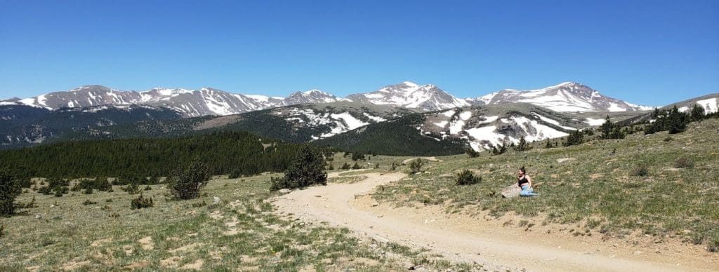 Dirt winding its way into snowcapped mountains with a woman sitting on the side